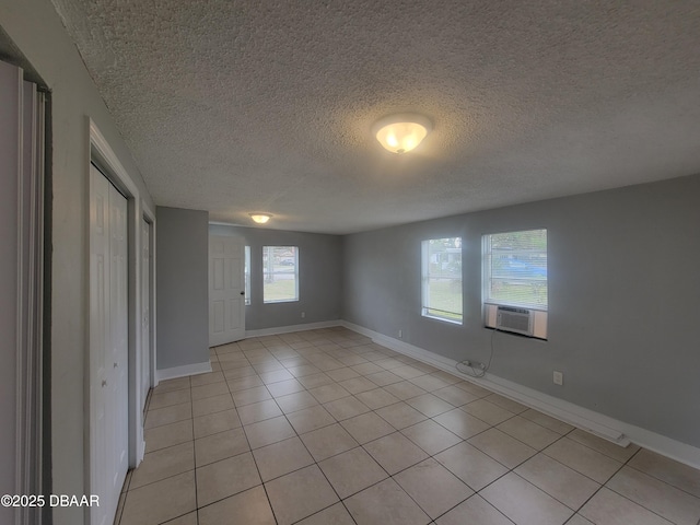 spare room featuring light tile patterned floors, cooling unit, baseboards, and a textured ceiling