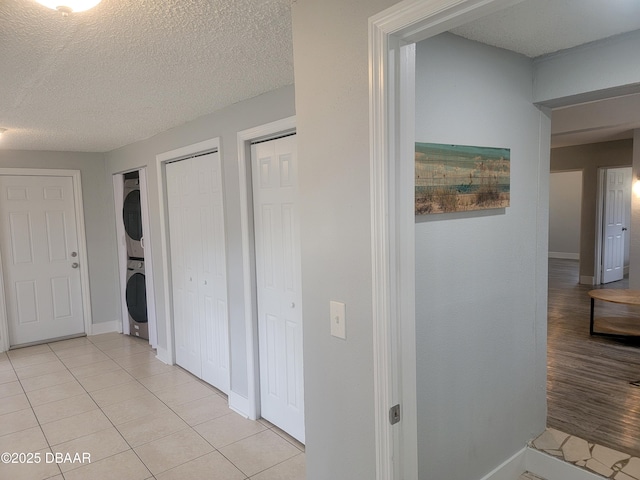 corridor with a textured ceiling, stacked washer / drying machine, and light tile patterned flooring