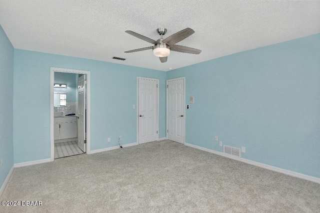 unfurnished bedroom with ensuite bathroom, light colored carpet, a textured ceiling, and ceiling fan