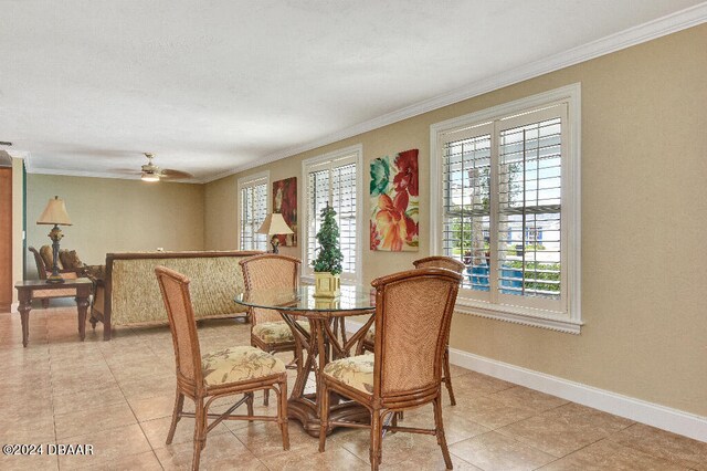 tiled dining space with ceiling fan and crown molding