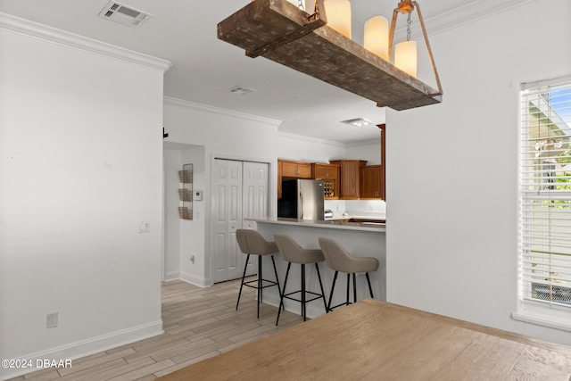 kitchen with kitchen peninsula, a breakfast bar, stainless steel refrigerator, pendant lighting, and light hardwood / wood-style flooring