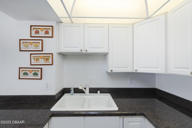 kitchen with dark countertops, white cabinets, and a sink