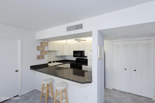 kitchen featuring visible vents, white cabinets, a peninsula, black appliances, and a kitchen bar