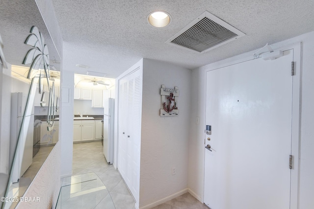 hallway featuring light tile patterned floors, visible vents, and a textured ceiling