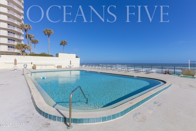 pool featuring a patio area, a water view, and fence