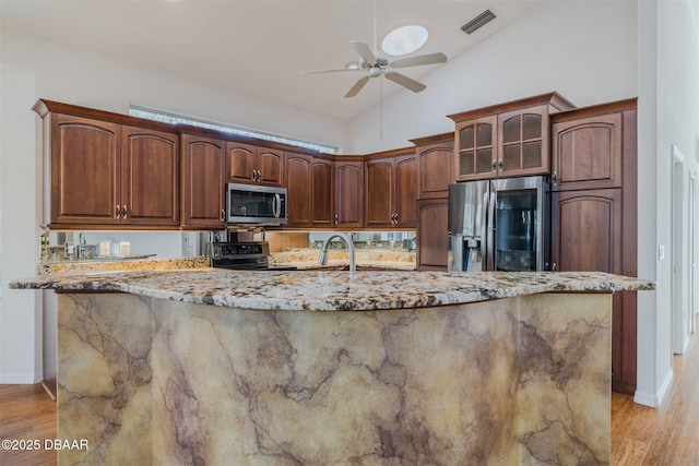 kitchen with ceiling fan, appliances with stainless steel finishes, light stone counters, and light hardwood / wood-style floors