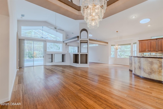 unfurnished living room with high vaulted ceiling, light hardwood / wood-style floors, and ceiling fan with notable chandelier