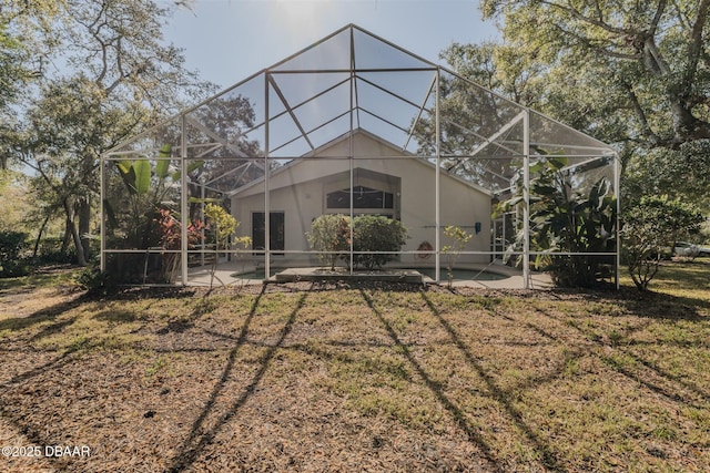 rear view of property featuring a yard, a patio area, and glass enclosure