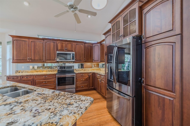 kitchen with light hardwood / wood-style flooring, ceiling fan, appliances with stainless steel finishes, light stone counters, and vaulted ceiling