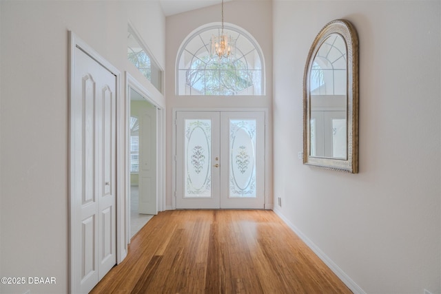 foyer entrance featuring french doors, a high ceiling, light hardwood / wood-style flooring, and a notable chandelier