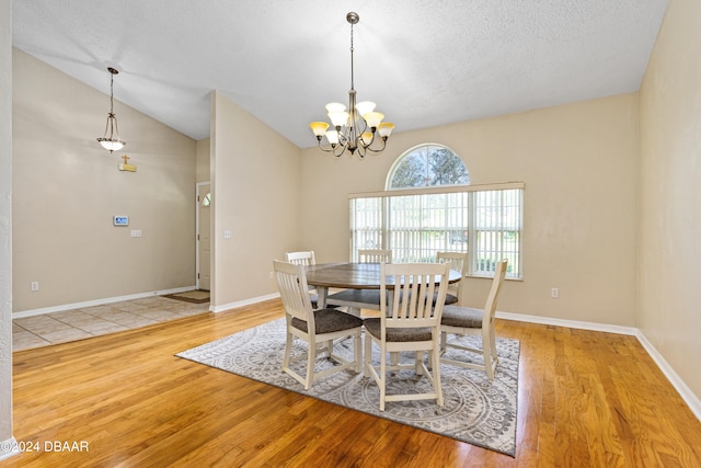 dining area featuring a chandelier, light wood-type flooring, lofted ceiling, and a textured ceiling