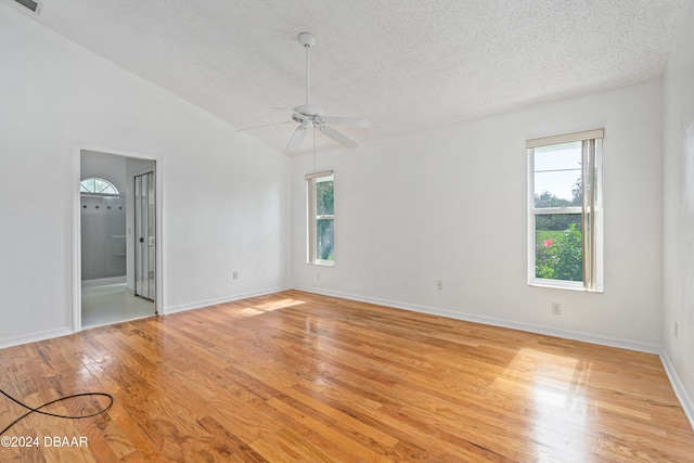 empty room featuring light wood-type flooring, vaulted ceiling, ceiling fan, and a textured ceiling