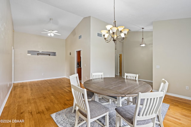 dining area with ceiling fan with notable chandelier, light hardwood / wood-style floors, and high vaulted ceiling