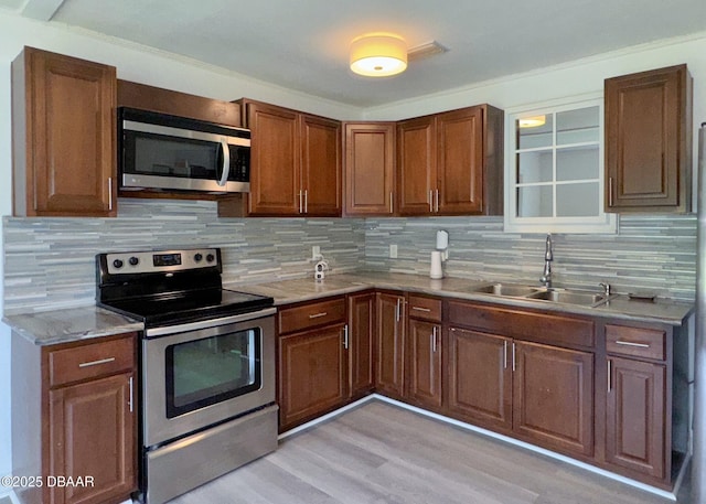 kitchen with light wood-style floors, a sink, decorative backsplash, and stainless steel appliances