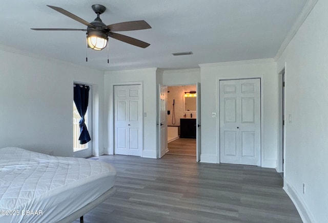 bedroom featuring crown molding, multiple closets, baseboards, wood finished floors, and visible vents
