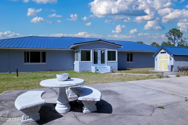 exterior space with an outdoor structure, a front lawn, stucco siding, metal roof, and entry steps