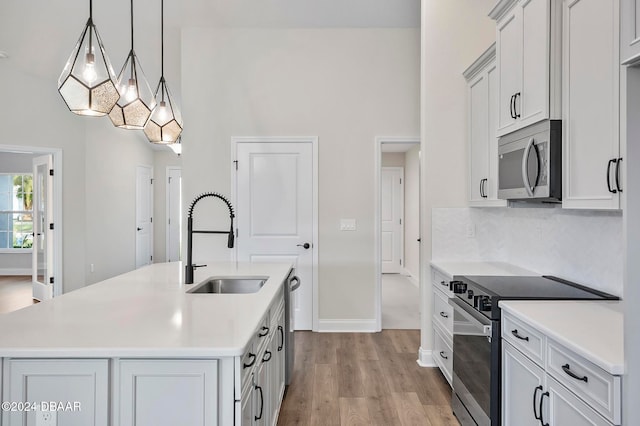 kitchen with stainless steel appliances, light wood-type flooring, pendant lighting, sink, and an island with sink