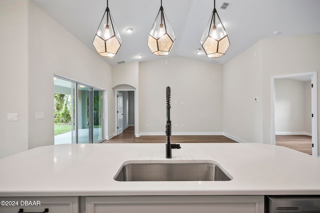 kitchen featuring sink, decorative light fixtures, an island with sink, wood-type flooring, and vaulted ceiling