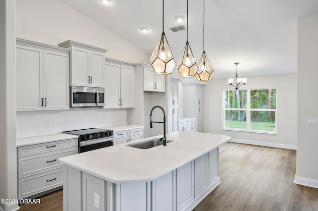 kitchen featuring stainless steel appliances, lofted ceiling, hanging light fixtures, sink, and a kitchen island with sink