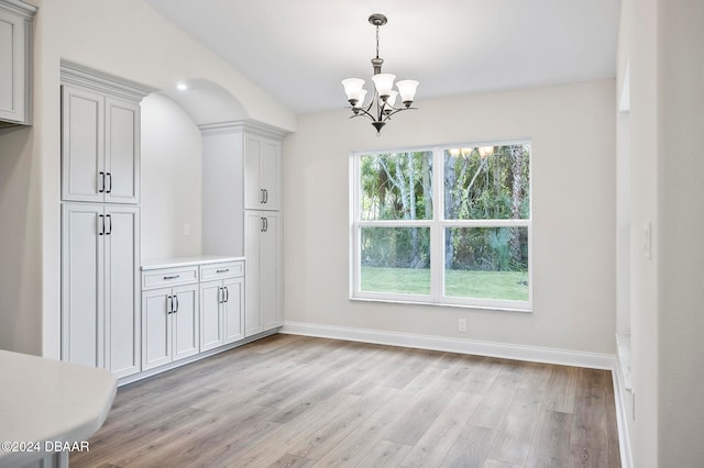 unfurnished dining area featuring light wood-type flooring and a notable chandelier