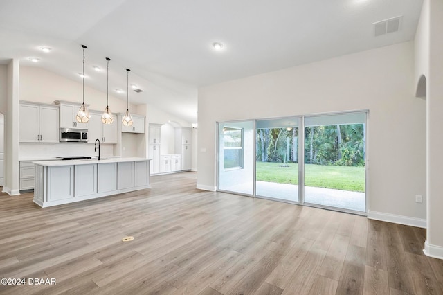 kitchen with a center island with sink, high vaulted ceiling, hanging light fixtures, sink, and light hardwood / wood-style floors