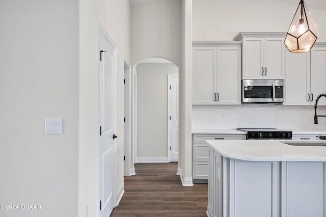 kitchen featuring pendant lighting, dark hardwood / wood-style floors, backsplash, white cabinetry, and appliances with stainless steel finishes