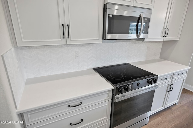 kitchen with white cabinetry, appliances with stainless steel finishes, hardwood / wood-style floors, and backsplash