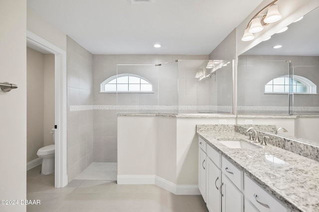 bathroom with tile patterned flooring, vanity, toilet, and a tile shower