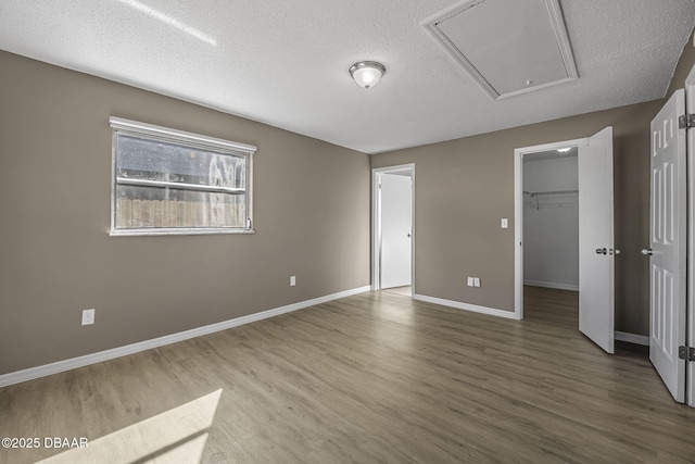 unfurnished bedroom with a walk in closet, hardwood / wood-style floors, a textured ceiling, and a closet