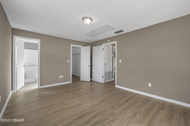 unfurnished bedroom with hardwood / wood-style floors, a spacious closet, connected bathroom, and a closet