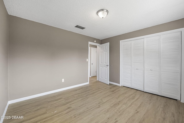 unfurnished bedroom with a textured ceiling, light wood-type flooring, and a closet