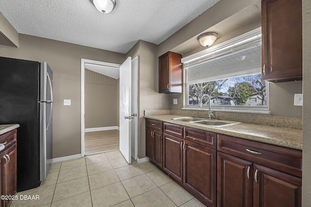 kitchen featuring sink, light tile patterned floors, stainless steel fridge, and a textured ceiling