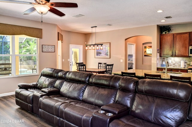 living room featuring dark wood-style floors, visible vents, a textured ceiling, and ceiling fan with notable chandelier