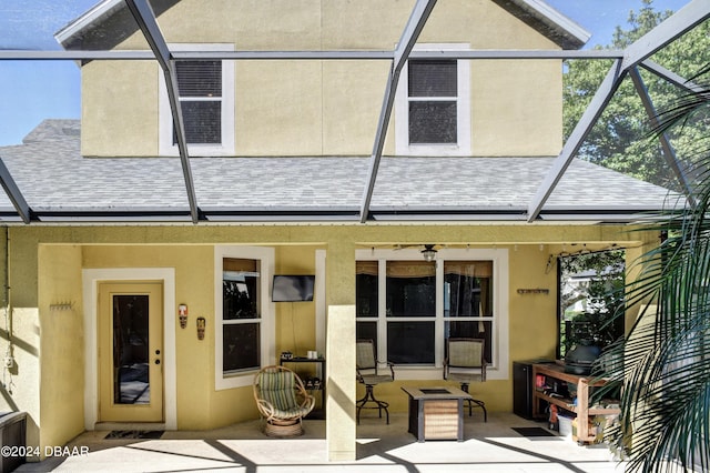 back of house featuring a lanai, stucco siding, a shingled roof, and a patio