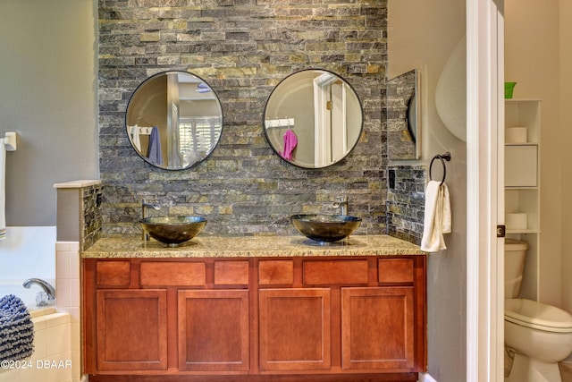 bathroom featuring toilet, a garden tub, double vanity, and a sink