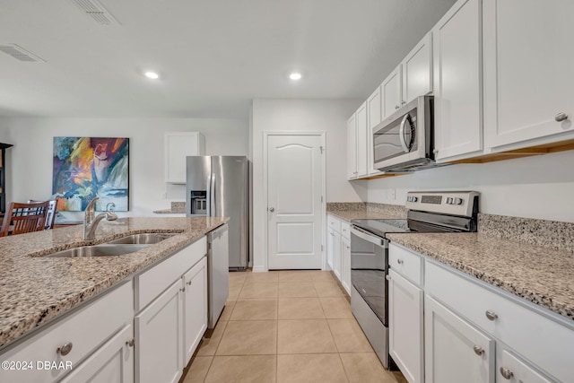 kitchen featuring stainless steel appliances, light tile patterned floors, light stone countertops, sink, and white cabinets