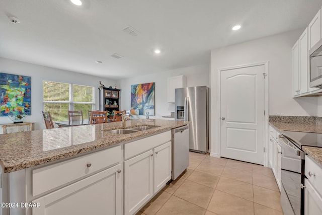 kitchen featuring stainless steel appliances, white cabinetry, light stone countertops, sink, and an island with sink