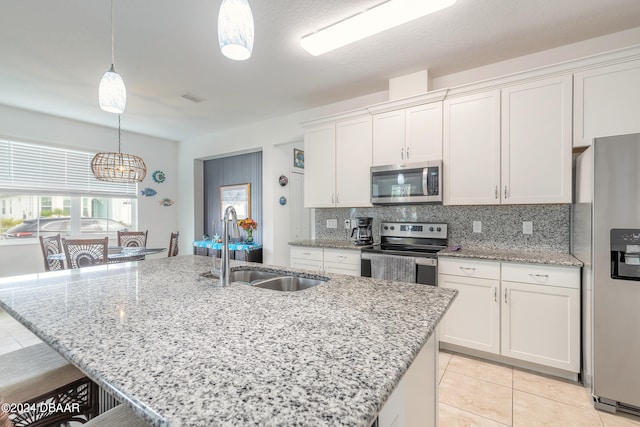 kitchen featuring stainless steel appliances, white cabinetry, a kitchen island with sink, and decorative light fixtures