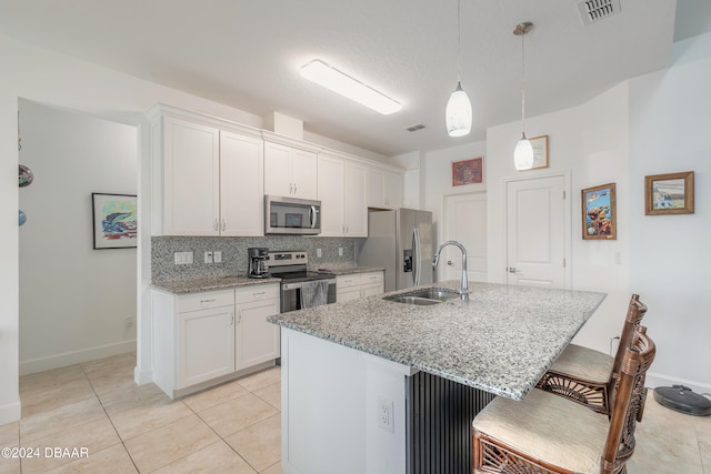 kitchen with a center island with sink, light stone counters, white cabinets, pendant lighting, and appliances with stainless steel finishes