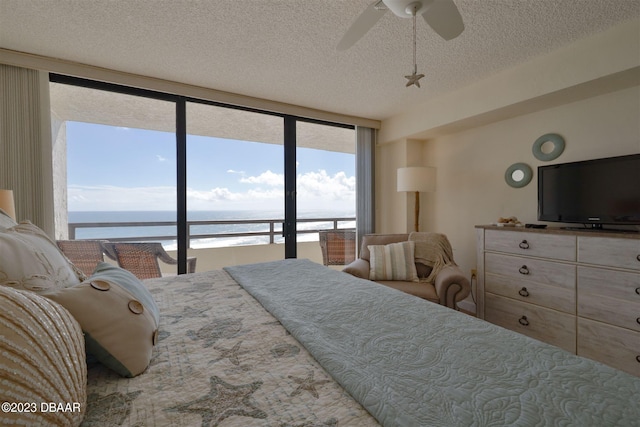 bedroom with access to outside, a water view, a textured ceiling, floor to ceiling windows, and ceiling fan