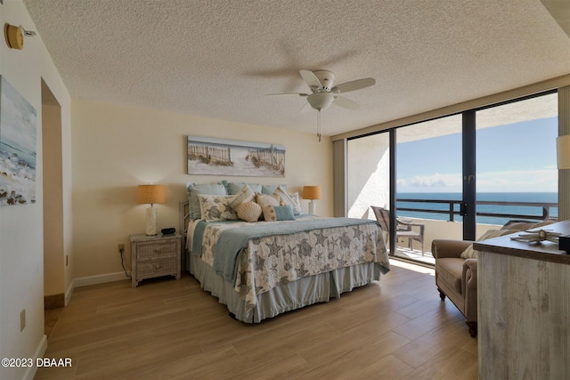 bedroom featuring access to outside, a water view, floor to ceiling windows, ceiling fan, and light wood-type flooring