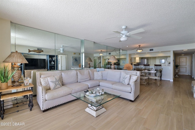 living room with light hardwood / wood-style floors, a textured ceiling, and ceiling fan