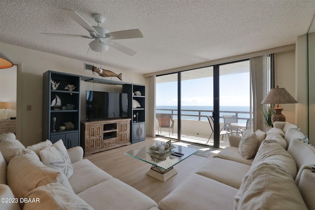 living room with a textured ceiling, light wood-type flooring, a wall of windows, and ceiling fan