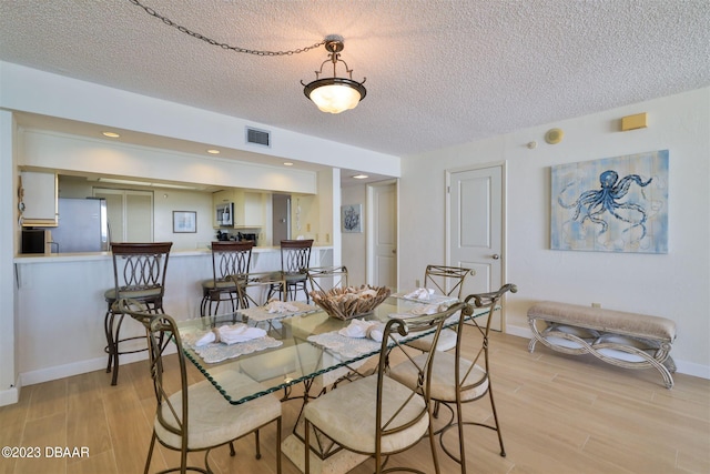 dining room featuring light wood-type flooring and a textured ceiling