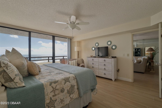 bedroom featuring access to outside, a textured ceiling, expansive windows, light hardwood / wood-style floors, and ceiling fan