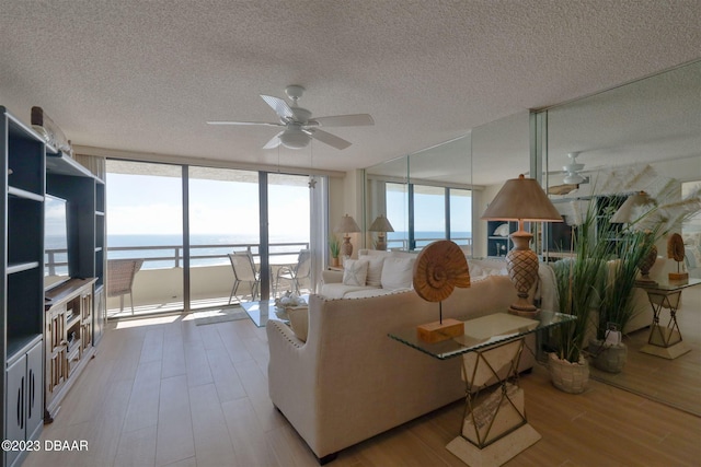 living room featuring a textured ceiling, light wood-type flooring, a water view, and ceiling fan