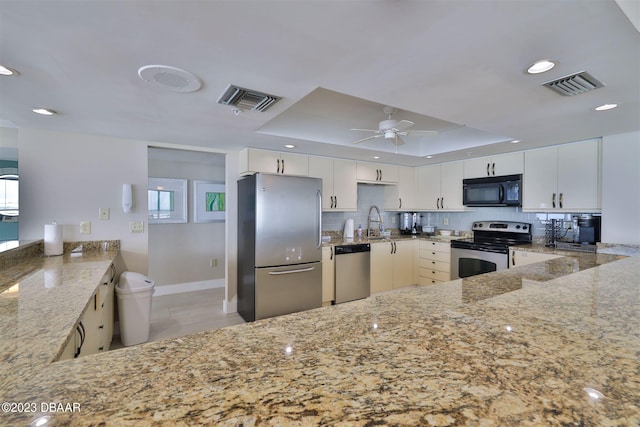 kitchen featuring sink, kitchen peninsula, appliances with stainless steel finishes, a tray ceiling, and white cabinets