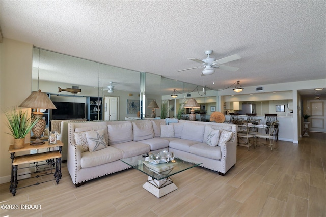 living room with light hardwood / wood-style floors, ceiling fan, and a textured ceiling