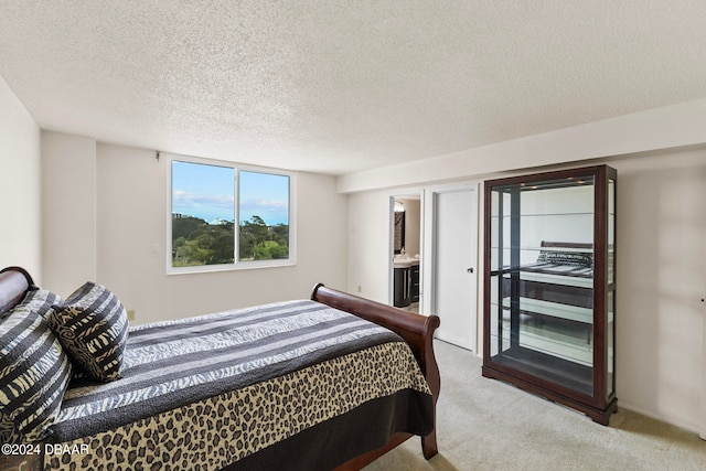 bedroom with a textured ceiling, light carpet, and ensuite bath