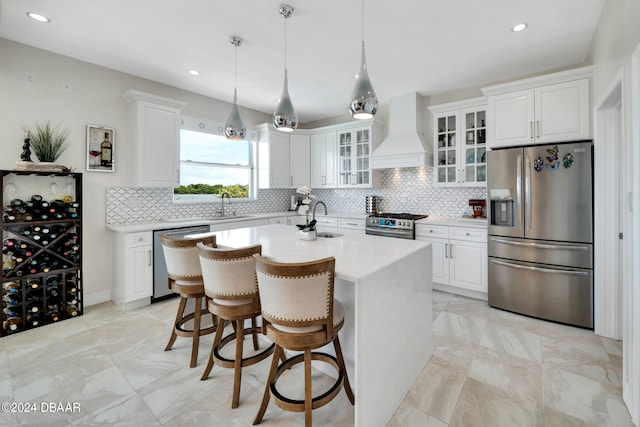 kitchen with white cabinets, custom range hood, appliances with stainless steel finishes, and a center island